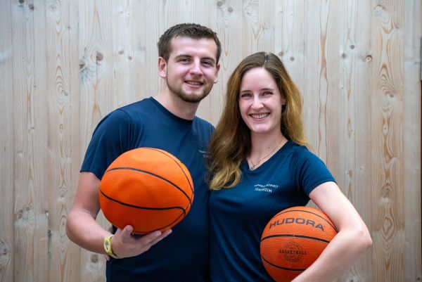 Mann und Frau mit Basketbällen vor einer Holzwand